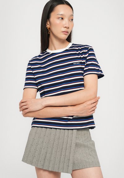 Gestreepte marineblauwe t-shirt met witte en blauwe strepen, ronde hals en klein logo. Gecombineerd met een grijze geplooide rok met speldjes.