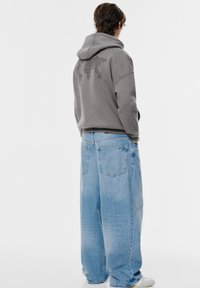 Grå huvtröja med en världskarta grafisk design på baksidan, i kombination med vida ljusblå jeans. Avslappnad design, lös passform.