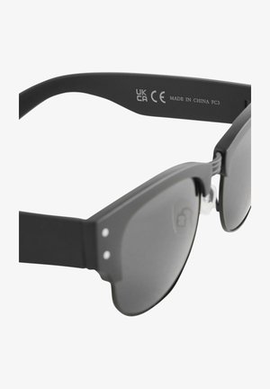 Zwarte zonnebril met een matte afwerking, voorzien van een uniek uitgesneden ontwerp, donkere lenzen en kleine zilveren accenten op het montuur.