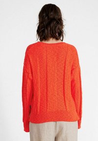 Maglione lavorato a maglia in oversize di un vivace arancione, con un motivo testurizzato, spalle cadenti e un orlo a coste. Vista posteriore mostrata.