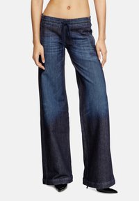 Pantalons en denim à jambes larges de couleur bleu foncé avec taille à cordon, présentant un dégradé fondu et des ourlets nets, associés à des talons aiguilles noirs.