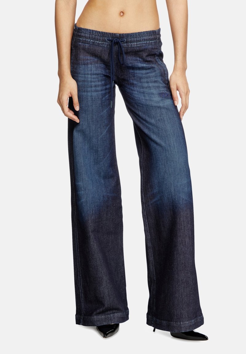 Pantalons en denim à jambes larges de couleur bleu foncé avec taille à cordon, présentant un dégradé fondu et des ourlets nets, associés à des talons aiguilles noirs.