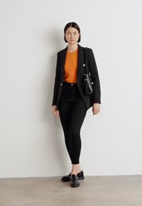 Svart blazer över en orange stickad topp, som är parat med högmidjade svarta byxor och svarta loafers. En liten svart handväska fulländar looken.