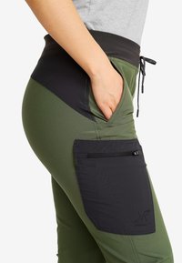 Featured product: green active pants with a black waistband. Notable details include a side pocket with a zipper and contrasting fabric textures.