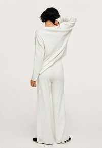 Biały sweter robiony na drutach o luźnym kroju i szerokich rękawach, w zestawie z pasującymi spodniami o szerokich nogawkach. Miękka tekstura i minimalistyczny design.