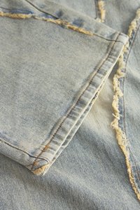 Ljusblå denimtyg med fransiga kanter, som visar en mjuk textur, kontrasterande sömmar och synliga sömdetaljer.