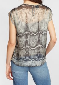 Lätt, genomskinlig blus med grå och beige ormskinnsmönster, korta ärmar och en nyckelhålsknäppning bak. Slät textur med ett flödande design.