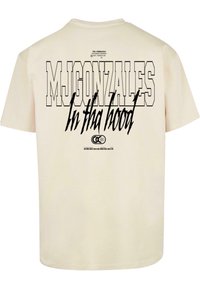 Short-sleeve, cream cotton t-shirt featuring large black graphic text on the back: "MJGONZALES In tha hood" with additional details below.