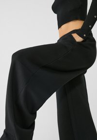 Zwarte wijde broek van zacht materiaal, met een hoge tailleband en zijzakken. Gladde textuur met strakke lijnen en een minimalistisch ontwerp.