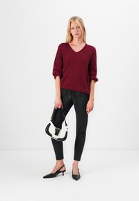 Bordeaux strikket sweater med V-udskæring, sorte pencilbukser med striber, sorte slingback hæle og en lille sort-hvid håndtaske med spænde.