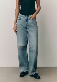 Lichtblauwe wijde jeans met een vervaagde wassing, met een hoge taille, vijf zakken en stikdetails. Gecombineerd met zwarte schoenen.
