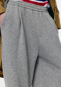 Sive trenirke s pregibom spredaj, z elastičnim pasom in mehko teksturo. Imajo stranske žepe in subtilne šive.