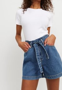 White ribbed t-shirt paired with high-waisted denim shorts featuring a tied waist, side pockets, and a classic blue wash texture.