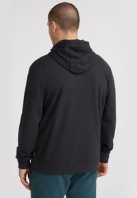 Sweat-shirt à capuche noir avec une coupe décontractée, des manches longues et des poignets côtelés. Le tissu semble doux et texturé, avec une étiquette de logo à l'ourlet.
