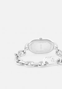 Zilverkleurige kettingarmbandhorloge met een ovale kast, waterdicht, sluiting met een haak, en gegraveerde details op de achterkant. Glanzende afwerking.