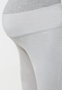 Lichtgrijze legging van rekbaar, soepel materiaal met een brede tailleband. De stof is aansluitend met een subtiele glans en een naadloos ontwerp.