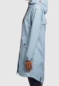 Giacca da pioggia azzurro chiaro con cappuccio, dotata di bottoni a pressione, tasca frontale e polsini regolabili. Realizzata in materiale impermeabile.