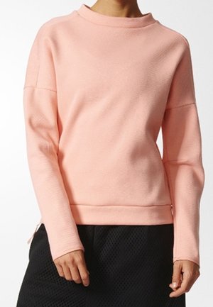 Person trägt einen langärmeligen, hellrosa strukturierten Pullover, kombiniert mit einem schwarzen strukturierten Rock vor einem schlichten weißen Hintergrund.