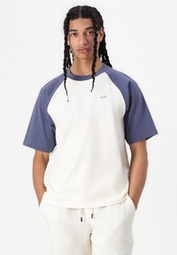 Camiseta de algodón blanca y marina con cuello redondo y mangas cortas. Presenta un pequeño logo en el pecho y un diseño de corte relajado.