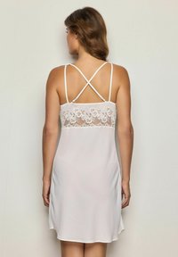 Camicia da notte bianca con dettaglio in pizzo sulla schiena, spalline incrociate regolabili, tessuto morbido e silhouette fluida con spacchi laterali.