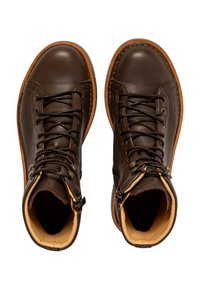 Botas de cuero marrón hasta el tobillo con punteras redondas, suelas en contraste en tono claro, cierre de cordones en el frente y detalle de cremallera lateral. Textura suave y diseño resistente.