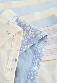 Pezzetti di tessuto di cotone in blu chiaro, crema e rosa tenue. I modelli comprendono righe e disegni floreali con cuciture e trame visibili.
