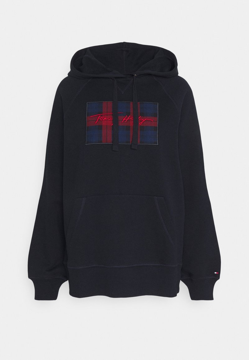 Haut à capuche bleu marine avec une poche kangourou et un cordon de serrage ajustable. Présente un patch en tartan rouge et bleu avec "Tommy Hilfiger" imprimé en rouge.
