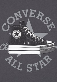 Illustrasjon av svart høytopp sneaker på grå bakgrunn, med hvite øyeletter, lisser, og en sirkulær logo med stjerner, samt fet tekst.
