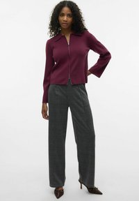 Burgundy zip-up tröja med krage, i kombination med grå rutiga vida byxor och bruna spetsiga skor med dekorativa nitar.