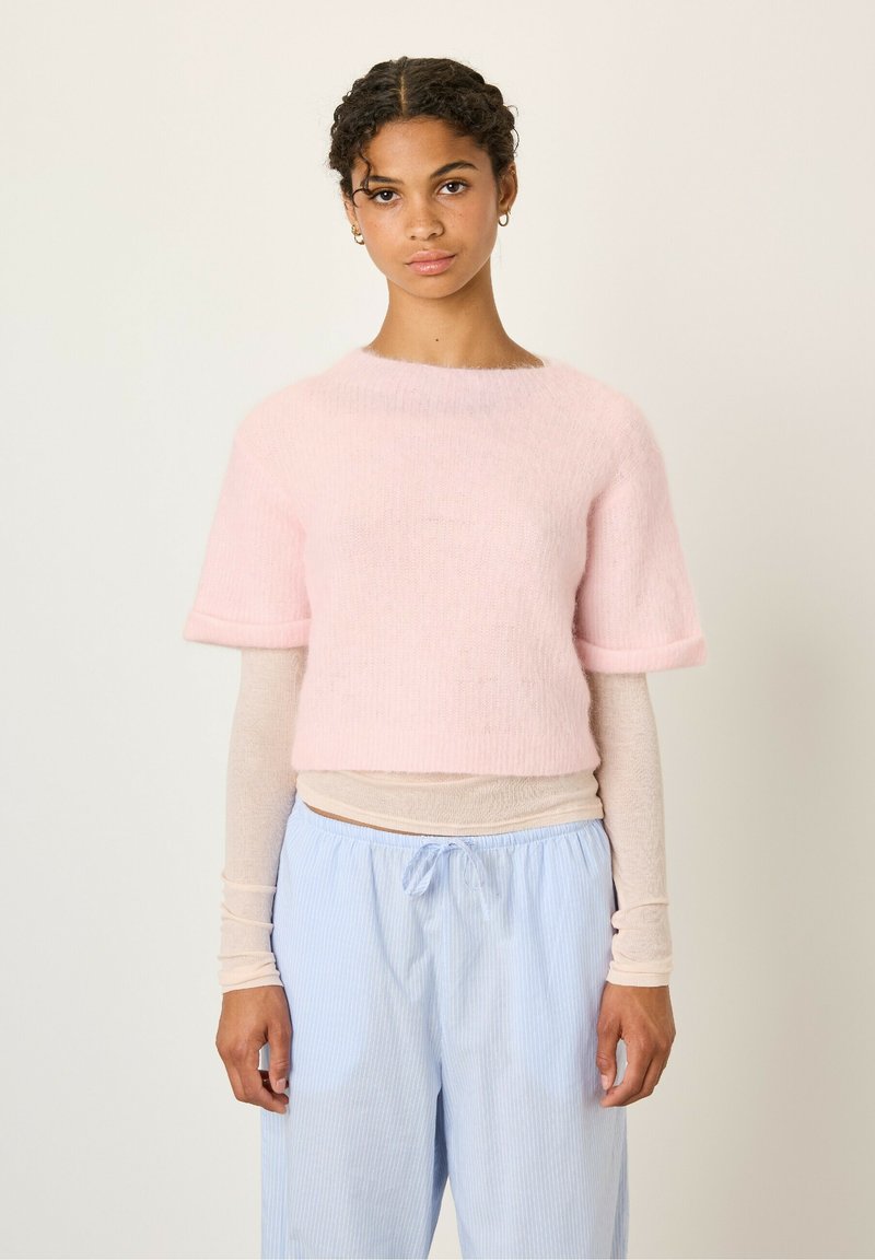 Korte roze mohairtrui met korte mouwen en contrasterende ribbelmanchetten, gepaard met lichtblauwe gestreepte broek en een licht lange mouw top daaronder.