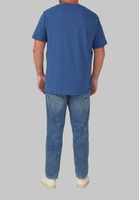 Niebieska koszulka z okrągłym dekoltem o luźnym kroju, zestawiona z jasnoniebieskimi dżinsami i białymi sneakersami, widok z tyłu.