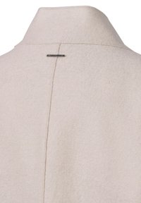 Helle beige Wolljacke mit einem hohen Kragen, ausgestattet mit einer Mittelnaht und einer kleinen metallischen Akzentnadel auf dem Rücken. Weiche Textur.