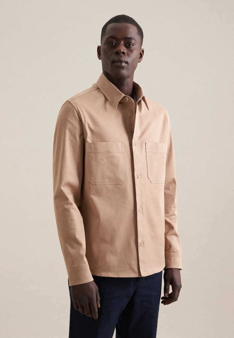 Camicia a maniche lunghe di colore marrone chiaro con chiusura a bottoni, dotata di due tasche sul petto e colletto strutturato, realizzata in un tessuto liscio.