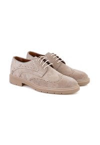 Chaussures en cuir suédé beige avec un design brogue classique, présentant des perforations décoratives et une semelle en caoutchouc rembourrée pour le confort.
