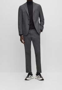Szary garnitur o fakturowanym wykończeniu, jednorzędowa marynarka, dopasowane spodnie i czarny golf. Do tego czarno-białe sneakersy.