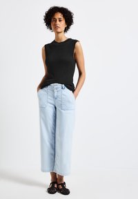 Top nero senza maniche in tessuto a costine, jeans a gamba larga azzurri chiari con tasche frontali e sandali neri intrecciati. Design semplice e casual.