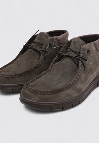 Chaussures en daim marron foncé avec un bout arrondi, des détails cousus et des lacets marron, présentant une surface texturée et une semelle en caoutchouc.