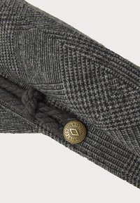 Grå mønstret stofaccessorie med en flettet detalje og en messingknap med et diamantdesign. Tekstureret og visuelt detaljeret.