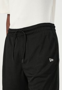 Black mesh athletic shorts with an elastic waistband, adjustable drawstring, and a small white logo accent on the left side.