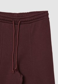 Pantaloni sportivi bordeaux con waistband elasticizzato e cordoncino, caratterizzati da una superficie liscia e tasche laterali.