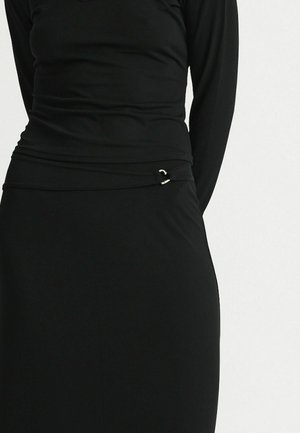 Nahaufnahme eines schwarzen, eng anliegenden Langarmoberteils und eines passenden Rocks mit einem kleinen silbernen Verschlussdetail an der Taille.