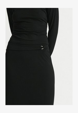 Close-up van een zwarte, nauwsluitende top met lange mouwen en een bijpassende rok met een klein zilveren gespdetail ter hoogte van de taille.