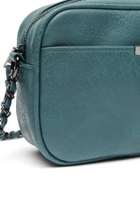 Borsa a tracolla in pelle teal con superficie liscia, angoli arrotondati e tracolla in catena nera. Presenta una chiusura a zip e un accento logo discreto.