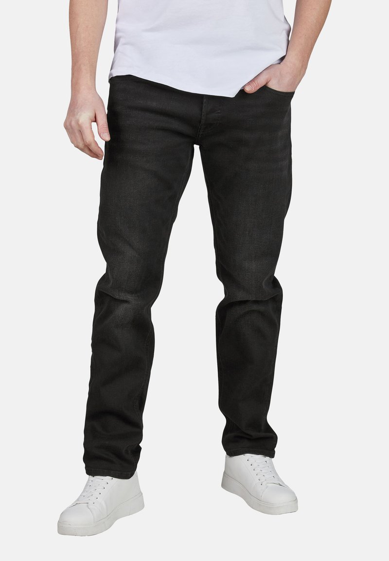 Jeans de denim negro con un ajuste estándar, que cuentan con cinco bolsillos, una textura sutil y detalles de costura, combinados con zapatillas blancas.