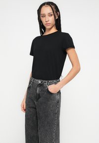 Fekete rövid ujjú póló, magas derekú, kopott fekete farmerrel párosítva, elülső zsebekkel és gombos záródással. Sima pamut anyag.