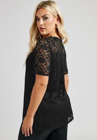 Top nero con maniche corte in pizzo con motivi floreali, scollatura rotonda e dettaglio a chiusura a chiave sul retro. Tessuto morbido.