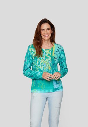 Türkiser gestrickter Pullover mit Blumen- und Sternmustern, rundem Halsausschnitt, langen Ärmeln und geripptem Saum. Kombiniert mit hellblauen, distressed Jeans.