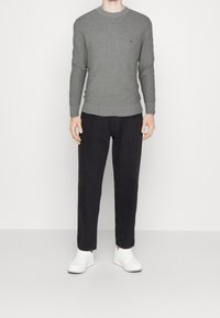 Pull gris en maille avec col rond, associé à un pantalon noir et des baskets blanches. Petit logo distinctif sur le pull. Design simple et texturé.