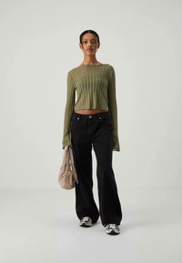 Olive green ribbed long-sleeve crop top, black wide-leg jeans, and white sneakers. Model holds a light beige bag. Neutral background.