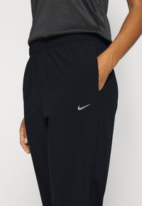 Sort træningsbukser lavet af letvægtsstof, med en tapered pasform, elastisk talje, sidelommer og et lille sølvlogo.